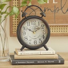 an alarm clock sitting on top of books next to a vase with flowers in it