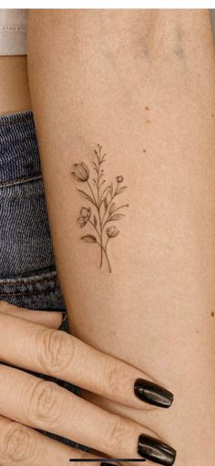 a small flower tattoo on the left side of the thigh, with two fingers holding it