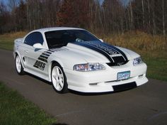 a white sports car parked on the side of a road with trees in the background