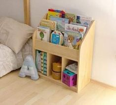 a wooden book stand with books and toys in it on the floor next to a bed