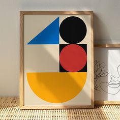 two framed art pieces sitting next to each other on top of a wooden table with a white wall in the background