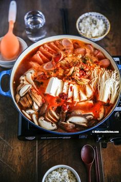 a large pot filled with lots of food on top of a wooden table next to utensils