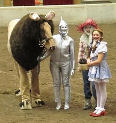 three children are standing next to a fake horse and other people dressed up in costumes