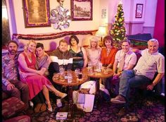 a group of people sitting around a table in a living room next to a christmas tree