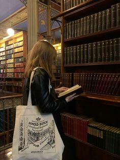 a woman is standing in front of bookshelves holding a book and looking at it