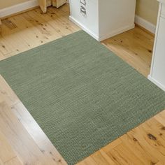 a green area rug in the middle of a wooden floor next to a white cabinet