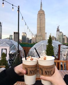 two people holding cups of ice cream in front of a cityscape with buildings and lights