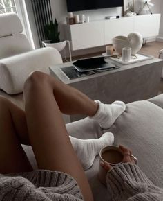 a woman is sitting on the couch with her legs crossed and holding a coffee cup