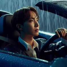 a young man sitting in the drivers seat of a car with rain pouring down on him