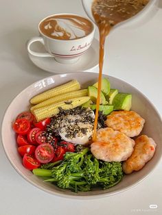 a white bowl filled with vegetables and meat next to a cup of coffee on top of a table