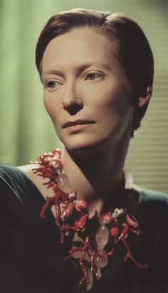 an older woman wearing a necklace with flowers on it's neck and looking off to the side