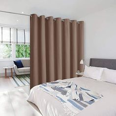 a white bed sitting next to a window covered in brown drapes on top of a hard wood floor