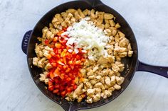 chicken, onions and peppers in a skillet on a white counter top with a blue spatula