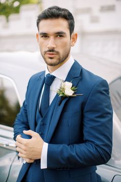 a man in a blue suit standing next to a car wearing a boutonniere