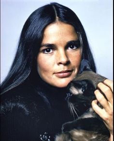 a woman holding a siamese cat in her right hand and looking at the camera