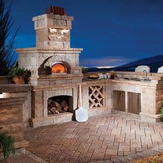 an outdoor pizza oven is lit up at night with lights on and brick patio area