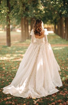 a woman in a wedding dress is walking through the grass with her back to the camera