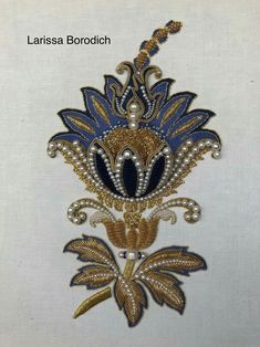 an embroidered brooch is shown on a white background with gold and blue accents,