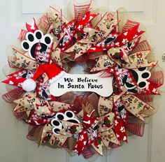 a red and white dog themed wreath on the front door with a sign that says, we believe in santa paws