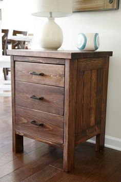 a wooden cabinet sitting on top of a hard wood floor next to a white lamp