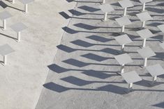 many chairs are arranged in the shape of squares on concrete flooring, with shadows cast by them