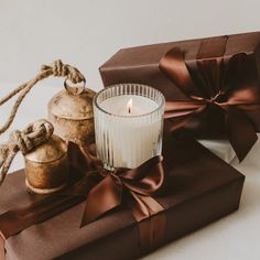 a lit candle sitting on top of a brown box next to two wrapped presents and a twine of twine