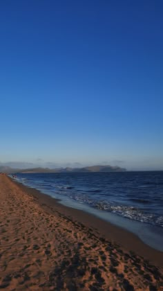 people are walking on the beach near the water and sand, with mountains in the distance