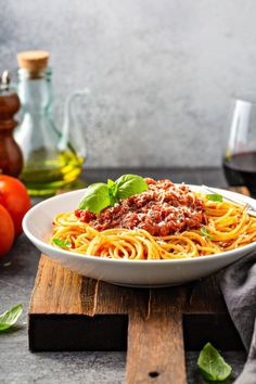 a white bowl filled with spaghetti and sauce on top of a wooden cutting board next to tomatoes