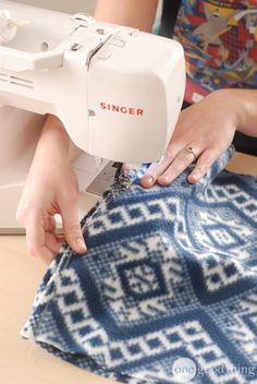 a woman is using a sewing machine to sew on a blue and white blanket