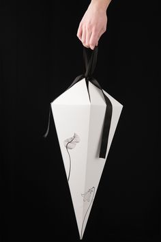 a person holding an origami box with black ribbon and flower design on it