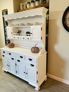 a white china cabinet sitting next to a clock