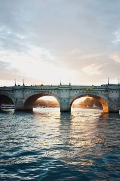 an old bridge over the water with boats on it at sunset or sunrise in the background