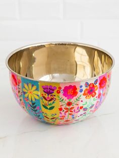 a metal bowl with colorful flowers painted on the side and gold in the bottom, sitting on a white surface