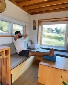 a man sitting on a couch in front of a window next to a wooden table