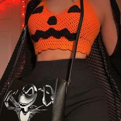 a woman in an orange crop top and black pants holding a handbag with a cat on it