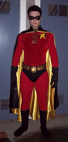 a man dressed in a red and gold costume standing next to a door with his hands on his hips