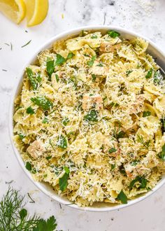 a white bowl filled with pasta covered in parmesan cheese and herbs next to lemon wedges