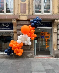 an orange, white and blue balloon arch on the side of a building in front of a store