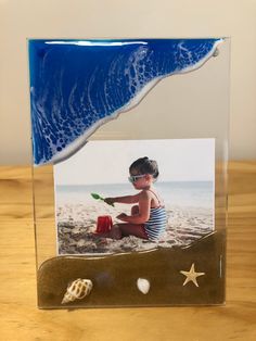 a glass frame with a photo of a boy on the beach and seashells