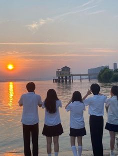 four people are standing on the shore watching the sun go down over the water with their backs to the camera