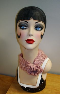 a mannequin with black hair and blue eyes wearing a pink scarf around her neck