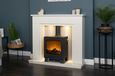 a white fireplace with a lit fire in the center and some plants on top of it