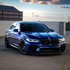 a blue bmw is parked in front of a building with clouds above it and the sun shining