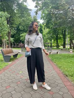 a woman standing in the middle of a park wearing black pants and a striped shirt