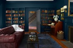 a living room with bookshelves, leather couch and coffee table in front of the fireplace