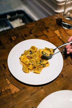 a person is eating pasta on a plate with a spoon in their left hand, while the rest of the table has plates and utensils