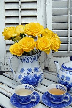 yellow roses are in a blue and white tea set