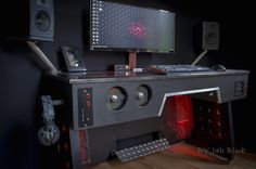 a computer desk with speakers and a monitor on it's side, in front of a black wall