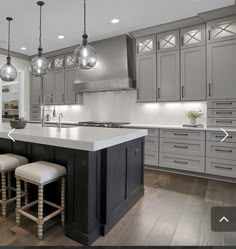 a large kitchen with gray cabinets and white counter tops, two stools at the center