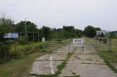 a road closed sign in front of a gated area with grass and bushes on both sides